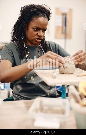 Reife Frau, die Ton formt, sitzt an einem Tisch im Kunstunterricht Stockfoto