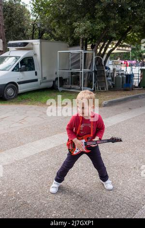 Netter kleiner Junge, der auf einem Festival sein Gitarrenspielzeug spielt Stockfoto