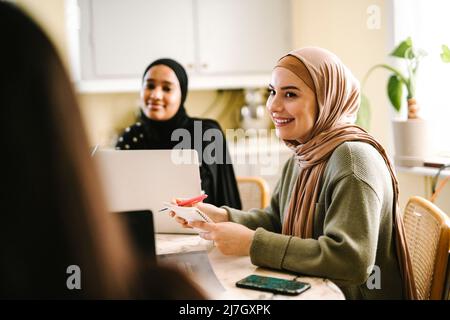 Lächelnde junge Frau im Hijab, die mit Freunden zu Hause studiert Stockfoto