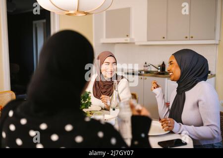 Glückliche junge Frauen in Hijabs beim gemeinsamen Abendessen zu Hause Stockfoto