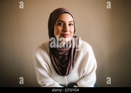 Lächelnde junge Frau in Hijab vor beigem Hintergrund Stockfoto