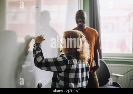 Seitenansicht des Jungen, der das mathematische Problem auf dem Whiteboard im Klassenzimmer löst Stockfoto