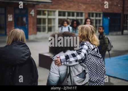 Junge, der mit dem Arm um einen Freund auf dem Schulgelände herumläuft Stockfoto