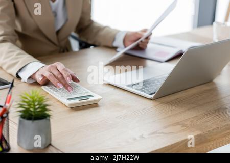 Teilansicht des Buchhalters mit Dokumenten, die den Rechner in der Nähe des Laptops verwenden Stockfoto