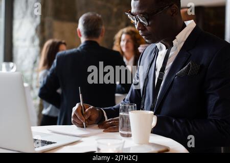 Geschäftsmann, der während des Seminars in einem Notizblock am Tisch schreibt Stockfoto