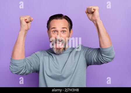 Portrait von schönen Mann mittleren Alters heben Fäuste im Sieg gewinnen Lotterie Geld isoliert auf violetten Hintergrund Stockfoto