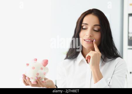 Frau hält Sparschwein, denken Sie an eine bessere Möglichkeit, Geld zu verwenden, um für die Zukunft zu sparen Stockfoto