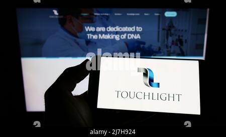 Person, die Mobiltelefon mit dem Logo des britischen Biotech-Unternehmens Touchlight Genetics Ltd. Auf dem Bildschirm vor der Webseite hält. Konzentrieren Sie sich auf die Telefonanzeige. Stockfoto