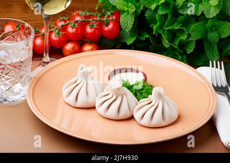 Khinkali – traditionelle georgianische Knödel, serviert mit einer Sauce aus saurer Rahm und Petersilie. Stockfoto