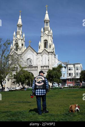 Der Mann mit einer Motorrad-Clubjacke von Hell's Angels geht mit seinem Hund vor die katholische Kirche der Heiligen Peter und Paul in San Francisco, Kalifornien. Stockfoto