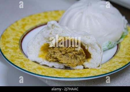 Halbgeöffnete chinesische Dampfbrötchen (cha siu bao) auf einem Teller, auf dem die Fleischvegetie-Füllung im Inneren zu sehen ist. Stockfoto