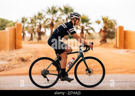 Seitenansicht des jungen Radfahrers auf dem Rennrad. Frau in Sportbekleidung und Helm auf dem Land trainieren. Stockfoto