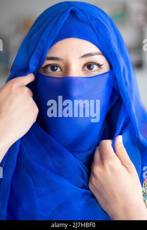 Porträt einer jungen muslimischen Frau, die einen Teil ihres Gesichts mit einem charakteristischen islamischen Schleier bedeckt. Nahaufnahme. Stockfoto