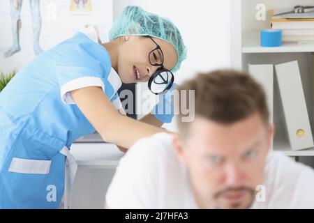 Frau Dermatologe untersuchen männlichen Patienten Körper, überprüfen Sie die Haut auf dem Rücken mit Lupe Stockfoto