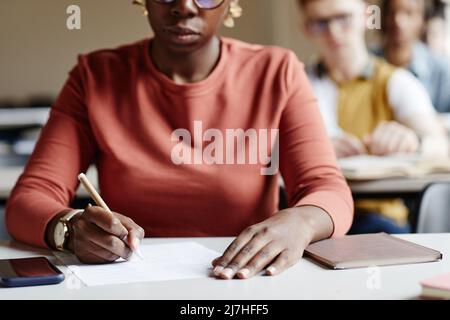 Nahaufnahme afroamerikanische junge Frau, die sich Notizen beim Lernen am Schreibtisch im College-Klassenzimmer gemacht hat Stockfoto