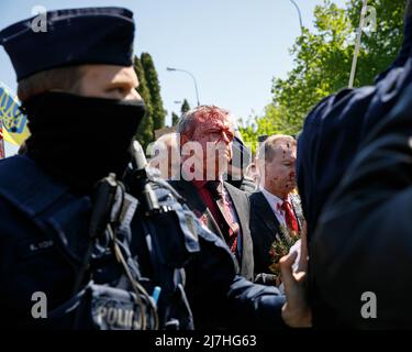 Warschau, Polen. 09.. Mai 2022. Der Botschafter der Russischen Föderation Sergej Andreew, umgeben von einem polnischen Polizeibeamten, bewegt sich in Richtung seines Autos, das mit gefälschtem Blut bedeckt ist. Am 77.. Jahrestag des Sieges der Roten Armee über Nazi-Deutschland traten ukrainische Aktivisten auf dem sowjetischen Soldatenfriedhof in Warschau auf, als sie gegen die russische Invasion in der Ukraine protestierten. Aktivisten verboten der russischen Delegation unter der Leitung von Sergej Andreev, dem Botschafter der Russischen Föderation in Polen, den Eintritt in den Friedhof. Während dieses Versuchs wurden Diplomaten von ukrainischen Aktivisten mit gefälschtem Blut übergossen. Stockfoto