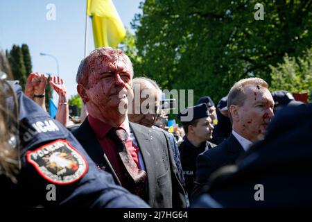 Warschau, Polen. 09.. Mai 2022. Der Botschafter der Russischen Föderation Sergej Andreew, umgeben von einem polnischen Polizeibeamten, bewegt sich in Richtung seines Autos, das mit gefälschtem Blut bedeckt ist. Am 77.. Jahrestag des Sieges der Roten Armee über Nazi-Deutschland traten ukrainische Aktivisten auf dem sowjetischen Soldatenfriedhof in Warschau auf, als sie gegen die russische Invasion in der Ukraine protestierten. Aktivisten verboten der russischen Delegation unter der Leitung von Sergej Andreev, dem Botschafter der Russischen Föderation in Polen, den Eintritt in den Friedhof. Während dieses Versuchs wurden Diplomaten von ukrainischen Aktivisten mit gefälschtem Blut übergossen. Stockfoto