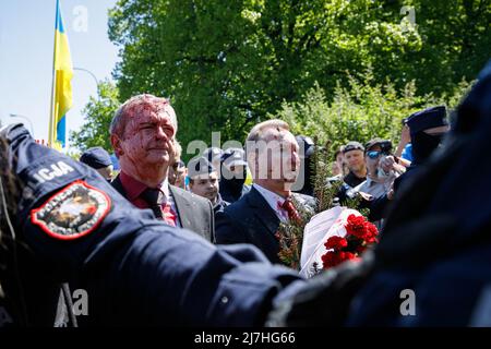 Warschau, Polen. 09.. Mai 2022. Der Botschafter der Russischen Föderation Sergej Andreew, umgeben von einem polnischen Polizeibeamten, bewegt sich in Richtung seines Autos, das mit gefälschtem Blut bedeckt ist. Am 77.. Jahrestag des Sieges der Roten Armee über Nazi-Deutschland traten ukrainische Aktivisten auf dem sowjetischen Soldatenfriedhof in Warschau auf, als sie gegen die russische Invasion in der Ukraine protestierten. Aktivisten verboten der russischen Delegation unter der Leitung von Sergej Andreev, dem Botschafter der Russischen Föderation in Polen, den Eintritt in den Friedhof. Während dieses Versuchs wurden Diplomaten von ukrainischen Aktivisten mit gefälschtem Blut übergossen. Stockfoto