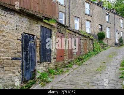 Steinhütten und gewundene gepflasterte Wege über der West-yorkshire-Stadt Holmfirth. Die Türen aus lackiertem Holz verbergen die ummauerten Schuppen, die früher zum Storen verwendet wurden Stockfoto