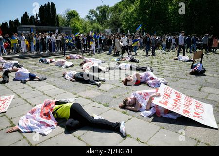 Warschau, Polen. 09.. Mai 2022. Während der Aufführung auf dem sowjetischen Soldatenfriedhof in Warschau am Tag des Sieges liegen Menschen auf dem Boden. Am 77.. Jahrestag des Sieges der Roten Armee über Nazi-Deutschland traten ukrainische Aktivisten auf dem sowjetischen Soldatenfriedhof in Warschau auf, als sie gegen die russische Invasion in der Ukraine protestierten. Aktivisten verboten der russischen Delegation unter der Leitung von Sergej Andreev, dem Botschafter der Russischen Föderation in Polen, den Eintritt in den Friedhof. Während dieses Versuchs wurden Diplomaten von ukrainischen Aktivisten mit gefälschtem Blut übergossen. Stockfoto