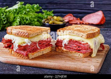 reuben Sandwich mit Roggenbrot dünn geschnittenes Corned Beef, Sauerkraut, tausend Inseln Dressing und geschmolzener Käse an Bord mit Gurken und Fleisch bei b Stockfoto