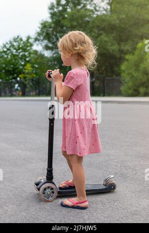 Kinderfahrroller. Kleines Mädchen, das im Sommer Zeit im Freien verbringt. Kind in einem Park. Stockfoto