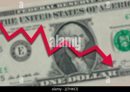 Eine US-Dollar-Rechnung verschwommen, während der Pfeil auf dem roten Aktienmarkt nach unten ging. Dollar-Wechselkurs geht nach unten Konzept. Stockfoto