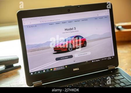 Griechenland, Athen, Januar 23 2022. TESLA FAHRZEUGAUSWAHL. Ad, online rot Tesla Modell 3 Elektro-Auto. Computer Laptop auf Holztisch, Nahaufnahme Stockfoto