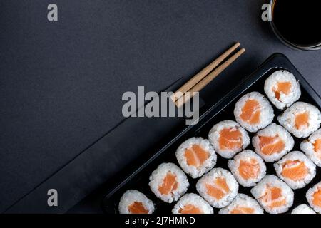 Lachs-Maki-Rolle auf schwarzem dunklen Hintergrund. Asiatisches Sushi-Maki-Set mit traditionellem Lachs, Draufsicht mit Kopierbereich Stockfoto