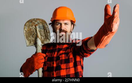 Builder in Schutzhelm und Arbeitshandschuhe mit Schaufel. Bärtiger Arbeiter in Harthut mit Spaten. Stockfoto