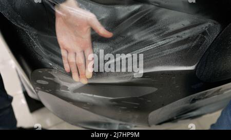 Autoverpackung mit Schutzfolie. Fahrzeugdetails. Verpackungsspezialist, der Vinylfolie oder Folie auf das Auto legt. Schutzfolie auf dem Auto. Anwenden eines Protecern Stockfoto