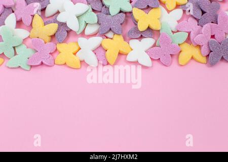 Bunte Schmetterlinge, beliebte Zuckerzuckerstreuseln, liegen auf einem rosa Hintergrund. Stockfoto