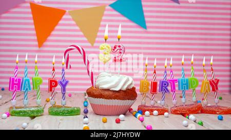 Happy Birthday Karte auf einem rosa Hintergrund, mit einer Figur in einem Cupcake. Schöner Happy Birthday Hintergrund mit einer Nummer mit brennender Kerze. Festlich Stockfoto