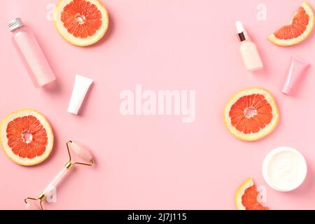 Rahmen aus Vitamin-C-Kosmetik und in Scheiben geschnittener Grapefruit auf rosafarbenem Hintergrund. Flach liegend. Stockfoto