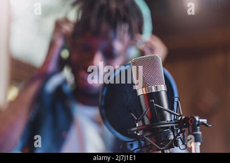 Kondensatormikrofon mit Antipop vor dem verschwommenen Gesicht eines Afrikaners, der live singt oder spricht - Technologiekonzept junger Menschen, die erschaffen Stockfoto