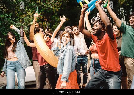 Vielfältige und verspielte Gruppe von jungen Menschen tanzen und Geselligkeit zusammen am Tag Gartenparty - Multigenerational freudige Familie genießen ihr ho Stockfoto