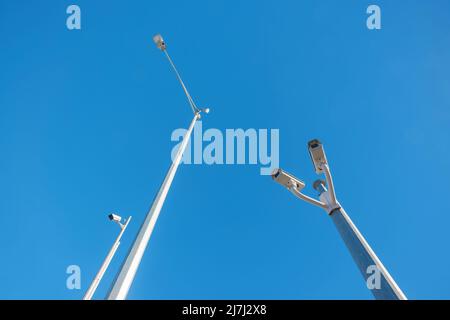 Ich schaue auf drei Überwachungskameras und Straßenlaterne vor einem klaren blauen Himmel Stockfoto