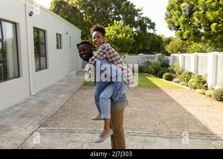 Porträt eines verspielten afroamerikanischen jungen Mannes, der eine junge Freundin huckepack, während sie im Hof steht Stockfoto