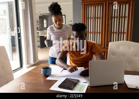 afroamerikanische junge Frau, die zu Hause bei einem ernsthaften Freund steht und Rechnungen auf dem Tisch analysiert Stockfoto