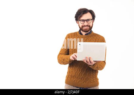 Ein zufriedener, gutaussehender, fröhlicher europäer in seinem 30s-er Alter, der einen gemusterten Pullover mit einem weißen Laptop trägt und auf die Kamera blickt. Hochwertige Fotos Stockfoto