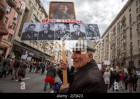 Moskau, Russland. 9.. Mai 2022. Der alte Mann hält Porträts von Josef Stalin und sowjetischen Marscharen armenischer Nationalität (von links nach rechts: Sergei Chudjakow, Iwan Isakow, Iwan Bagramyan, Hamasasp Babadschanian, Sergej Aganow), Während des Unsterblichen Regiments märz anlässlich des 77.. Jahrestages des Sieges im Zweiten Weltkrieg, in Moskau, Russland. Auf dem Banner steht: „Stalins Adler“ Stockfoto