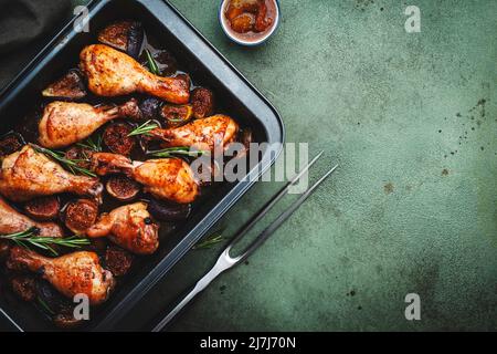 Gebackene Hähnchenbeine, Drumsticks mit süßen Feigen und Zwiebeln in balsamischer Marinade auf schwarzem Backblech, rostiger grüner Tischhintergrund, Draufsicht Stockfoto