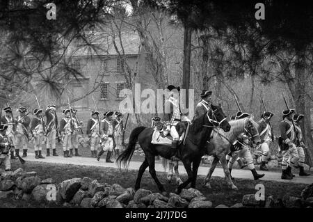 Reenactment Redcoat-Offiziere reiten ihre Pferde vor marschierenden Soldaten während der Simulation des Angriffs von den Redcoats auf der Battle Road in Lexi Stockfoto