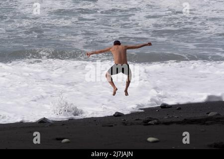 Ein nicht identifizierter Erwachsener spielt mit kaltem ozeanischem Wasser und Steinen, die am schwarzen Lavastrand auf der Insel La Palma, Kanarische Inseln, Spanien, springen Stockfoto