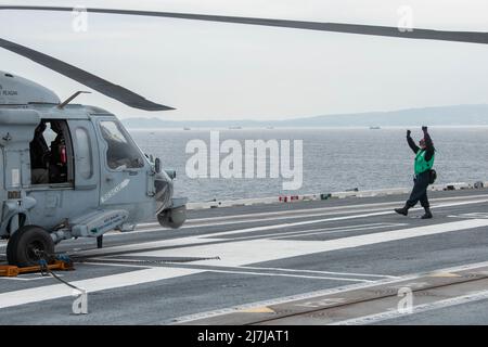 220508-N-BR419-1088 TOKYO BAY, Japan (8. Mai 2022) Mate Airman des Flugzeugmechanikers Dominique Mendez-Lopez aus Brandywine, Maryland, sendet Signale an die Piloten eines MH-60s Sea Hawk, der an den Golden Falcons of Helicopter Sea Combat Squadron (HSC) 12 befestigt ist, Auf dem Flugdeck des einzigen vorwärts eingesetzten Flugzeugträgers der US Navy USS Ronald Reagan (CVN 76). Ronald Reagan, das Flaggschiff der Carrier Strike Group 5, stellt eine kampfbereite Kraft zur Verfügung, die die Vereinigten Staaten schützt und verteidigt und Allianzen, Partnerschaften und kollektive maritime Interessen in der Indo-Pazifik-Region unterstützt. (USA Marineblau Stockfoto