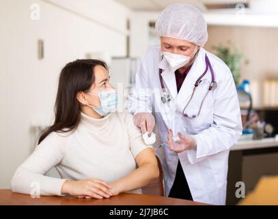 Fokussierte ältere Ärztin, die junge Frau impft Stockfoto