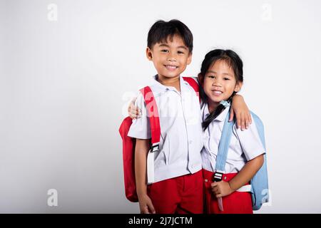 Zwei asiatische Student Kind Mädchen junge Schulkinder Bruder Schwester lächeln glücklich tragen Student thai uniform rote Hosen Rock umarmen einander isoliert auf weißen BA Stockfoto