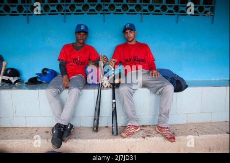 Kubanische Baseballspieler sitzen im Dugout und halten ihre Baseballschläger. Stockfoto