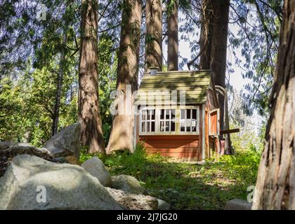 Holzspielhaus aus Holz. Braunes kleines Haus zwischen großen Bäumen. Holzmärchenbaumhaus, Spielhaus auf Kinderspielplatz. Niemand, Reise Stockfoto