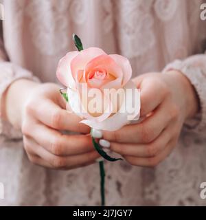 Weibliche Hand in rosa Bluse mit zarten rosa Rose. Minimalistisch trendige Komposition. Abstrakte Kunstidee. Romantische rosa Rosenblüte in Pastelltönen. Moderne Ästhetik. Neutrale Erdtöne. Kreative Grußkarte Hintergrund Vertikal Stockfoto